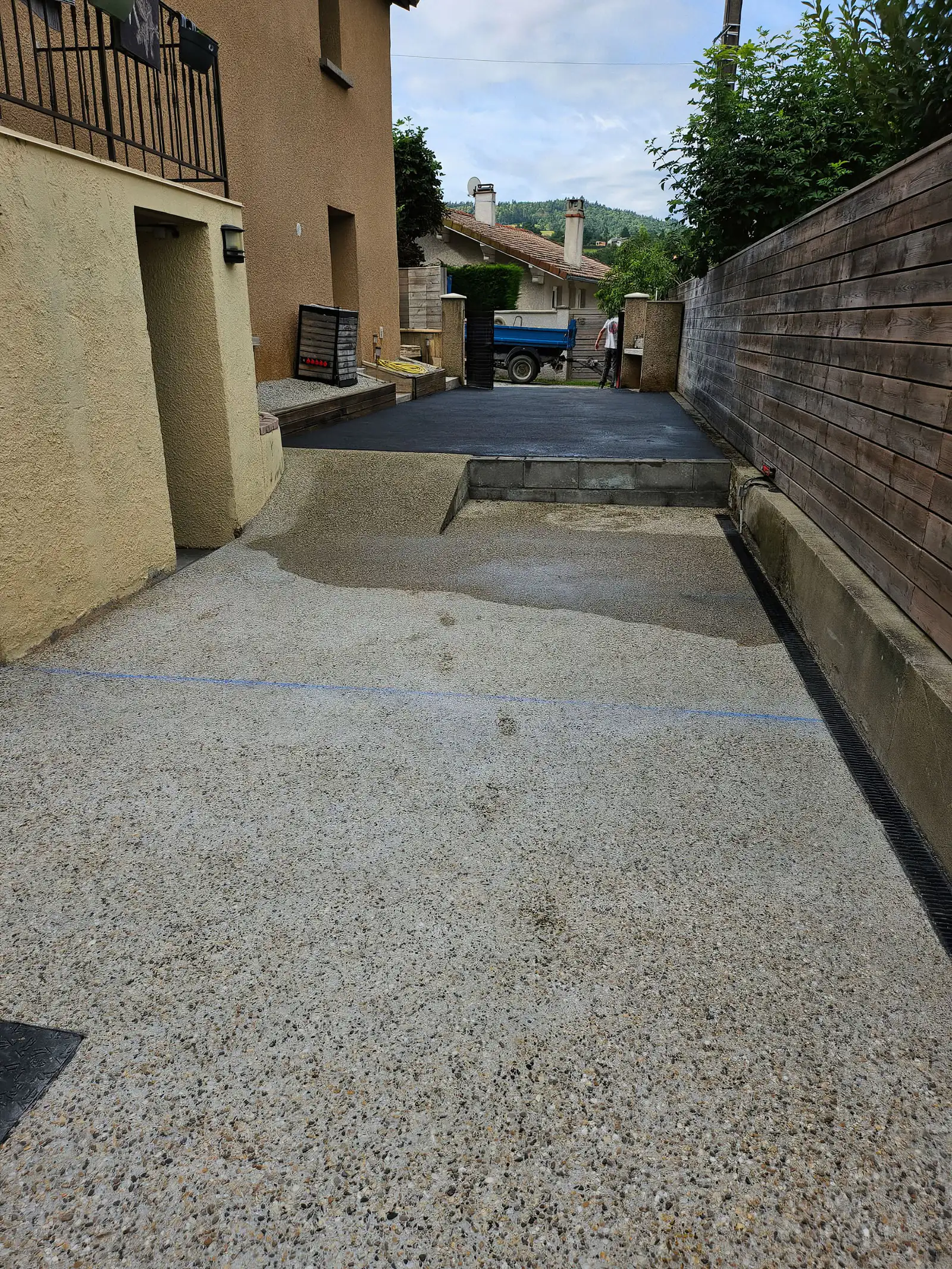 Allée en béton désactivé prolongée par une portion en enrobé, caniveau le long de la palissade