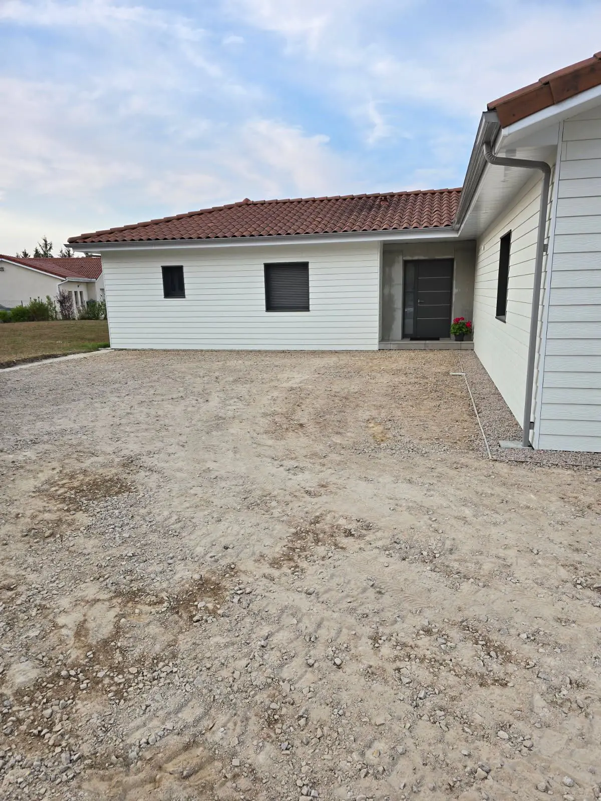 Avant travaux : cour en terre et gravier devant une maison neuve à bardage blanc