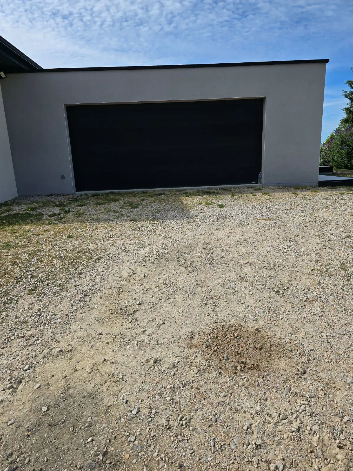 Avant travaux : cour en gravier usé devant un garage contemporain gris à porte noire