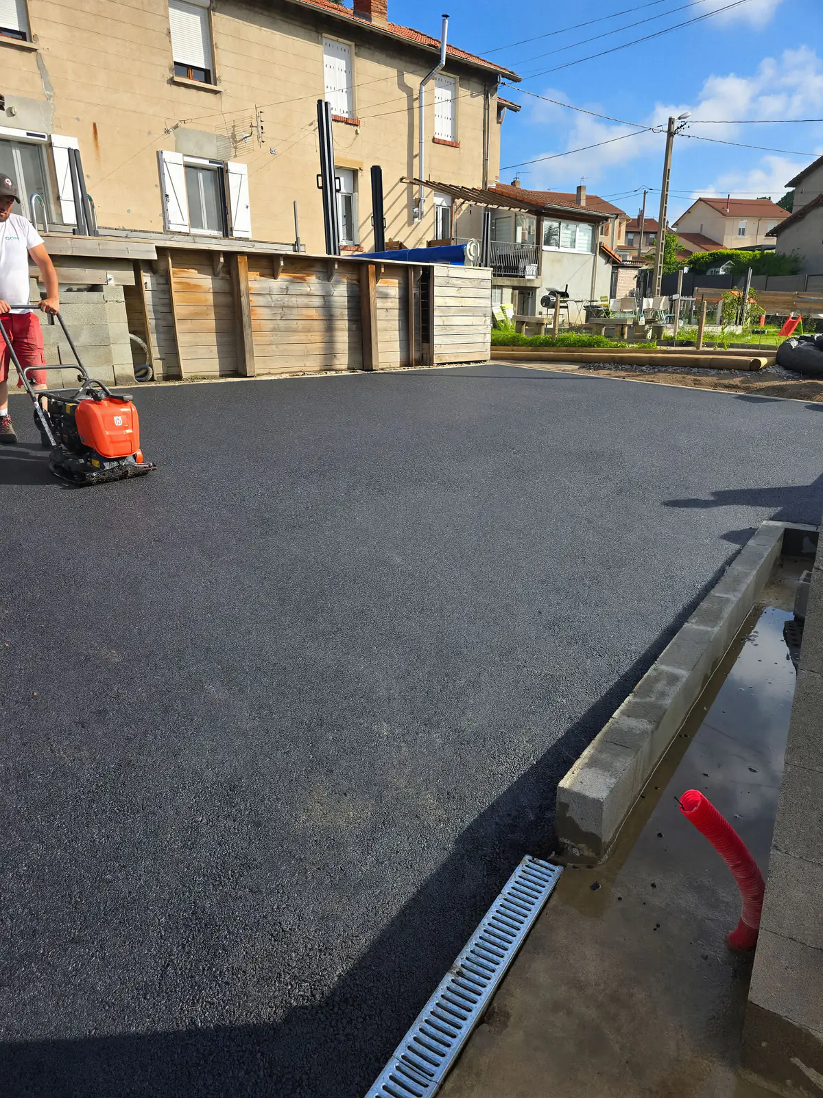 Compactage à la plaque vibrante d'une cour en enrobé neuf bordée d'un caniveau à grille