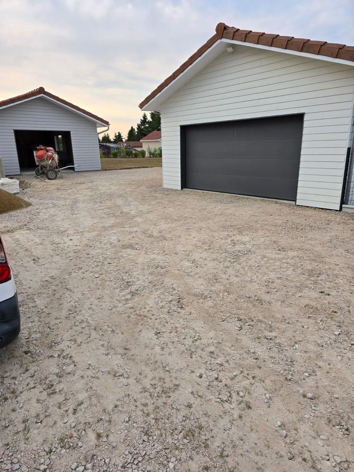 Avant travaux : plateforme en terre et gravier devant deux garages à bardage blanc